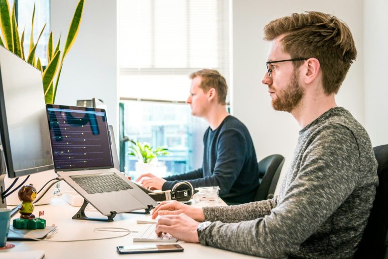 Kalkulation der Schäden am Kfz Zwei Männer arbeiten konzentriert an ihren Computern in einem modernen Büro.